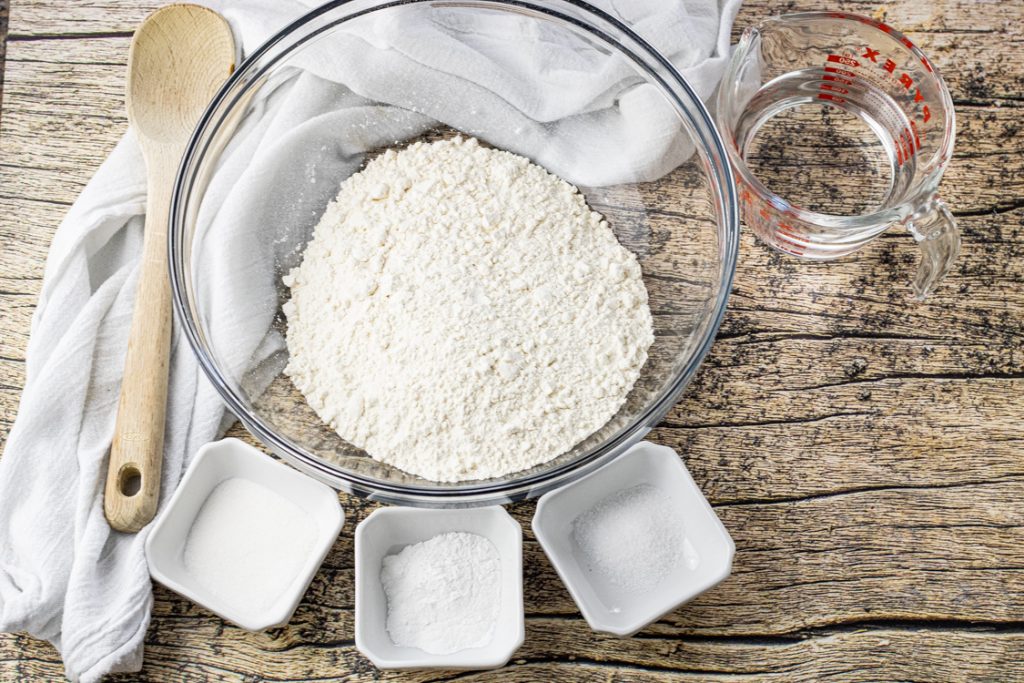 big glass bowl of flour surrounded by smaller bowls of sugar, salt and baking powder