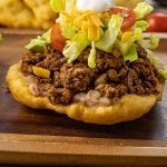 fry bread taco recipe topped with beans, meat, lettuce, cheese and sour cream