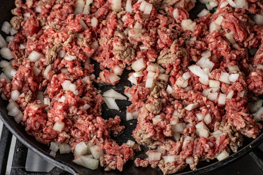 raw hamburger cooking with onions in a large skillet