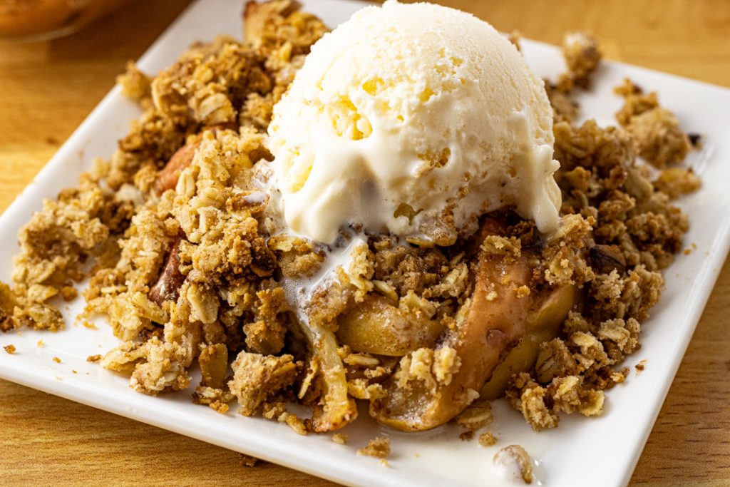 apple crisp on a white plate topped with vanilla ice cream