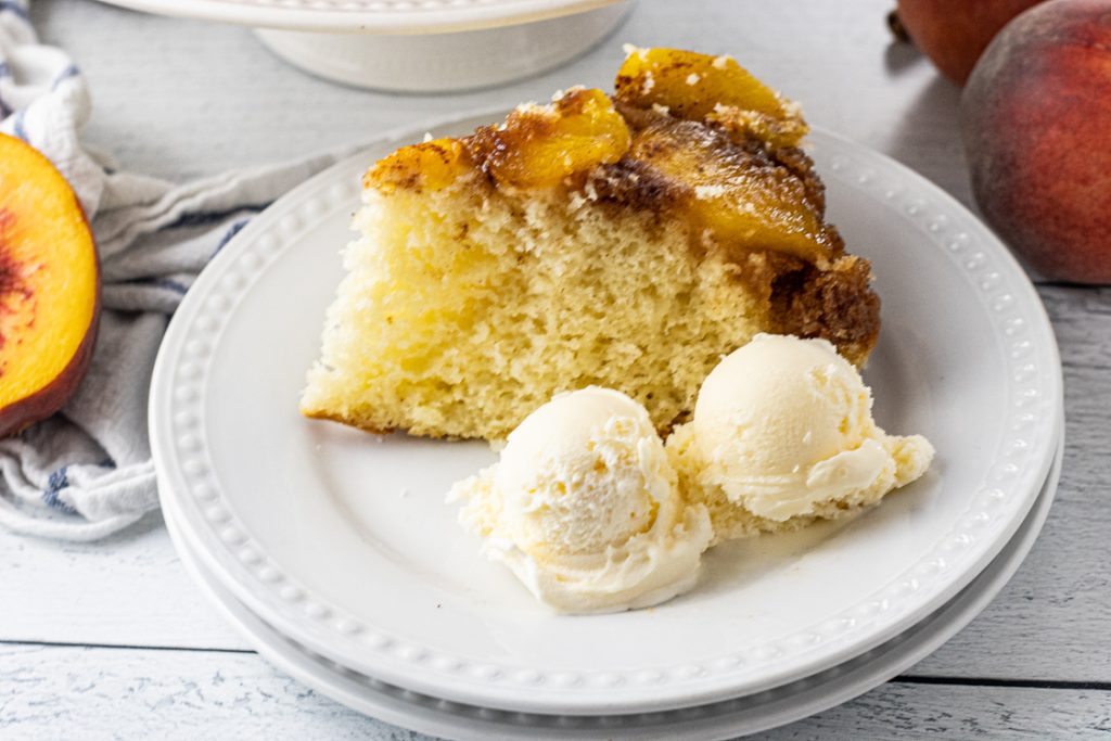 slice of peach upside down cake on a white plate with two scoops of vanilla ice cream