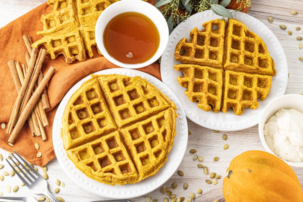 two white plates with orange colored pumpkin waffles on them.