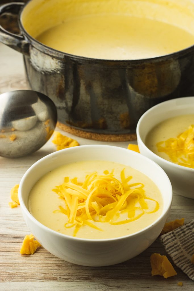 big pot of cauliflower cheese soup surrounded by a silver ladle and bowl fo the same soup