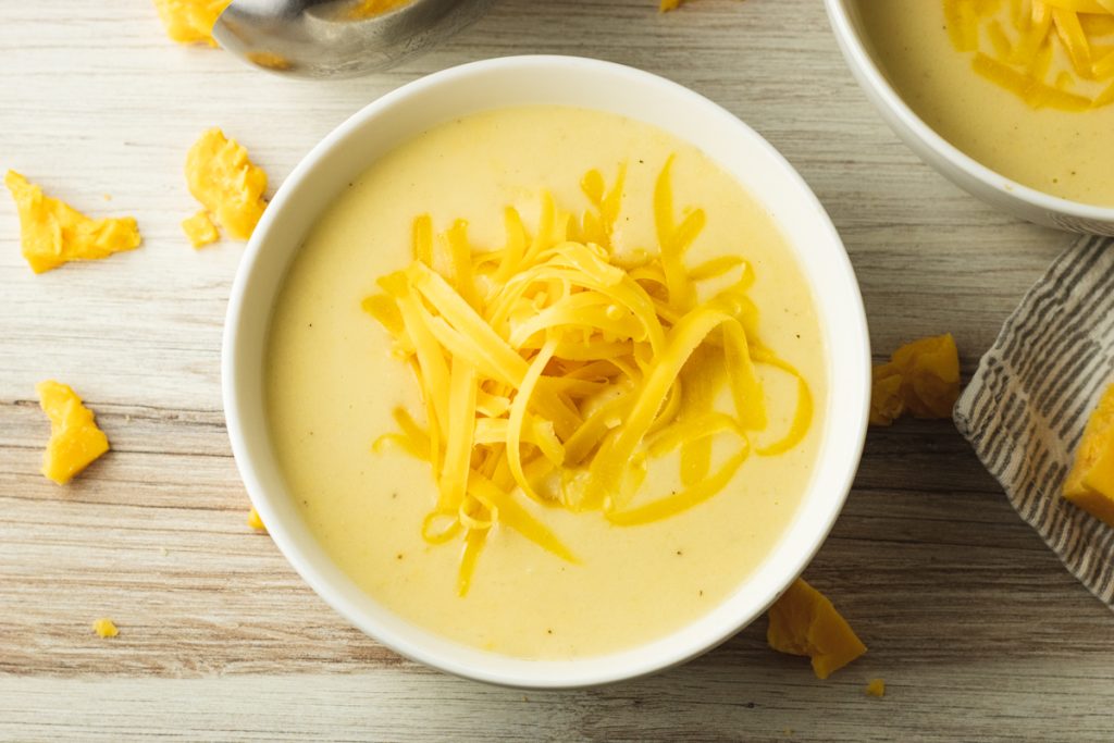 bowl of creamy cauliflower soup topped with shredded cheddar cheese.