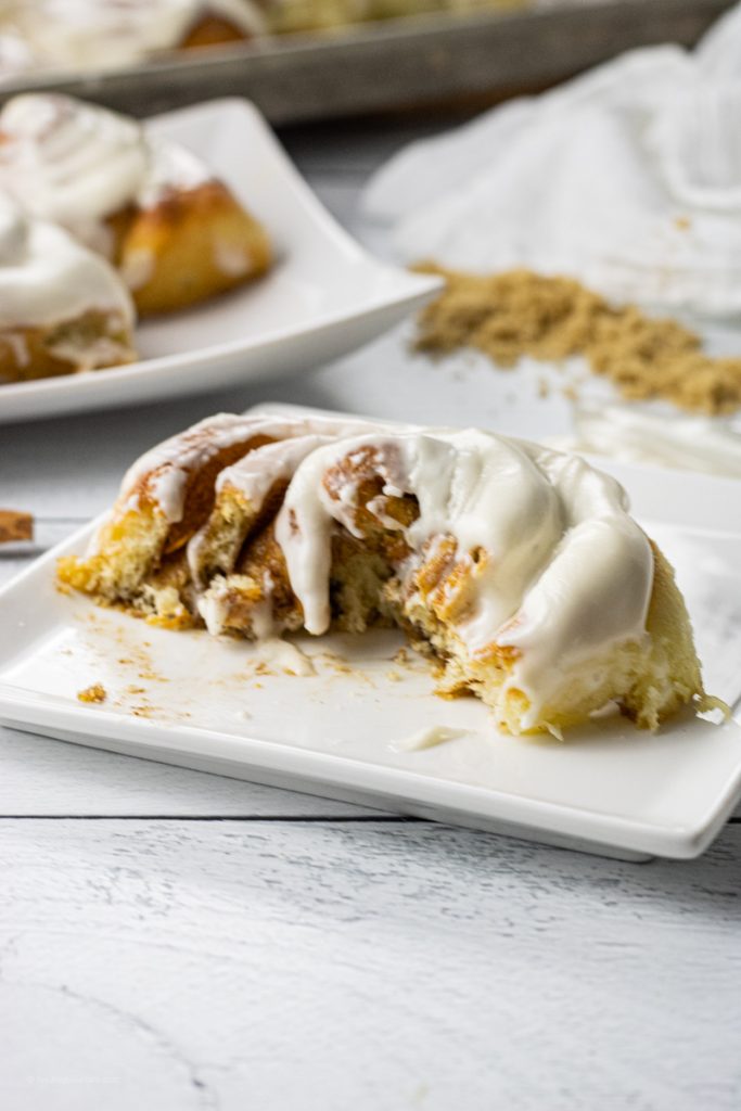 cinnamon roll cut in half with cream cheese frosting on a white plate