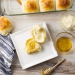 white dinner roll on a plate sliced in half with butter and honey