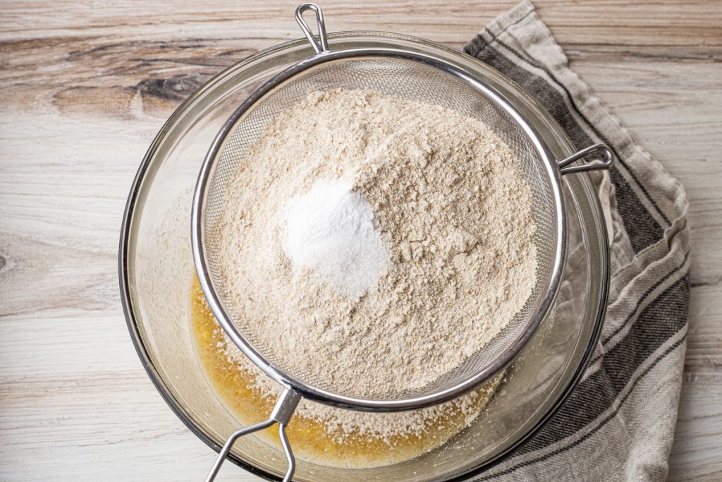 sifting dry ingredients into over a mixing bowl through a wire sifter