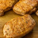 cooked, seasoned pork chops on a wooden cutting board