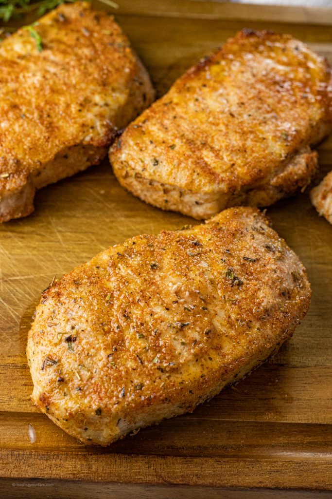 cooked, seasoned pork chops on a wooden cutting board