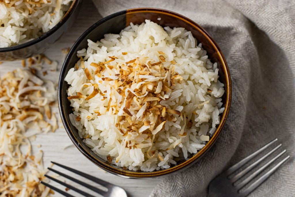 small brown bowl filled with coconut flavored rice topped with browned coconut