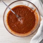 tomato sauce mixed with spices in a glass bowl with a mini whisk