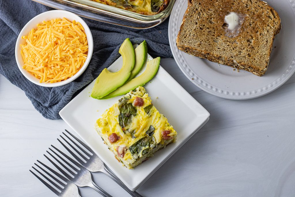 square piece of egg casserole on a white plate with avocado slices