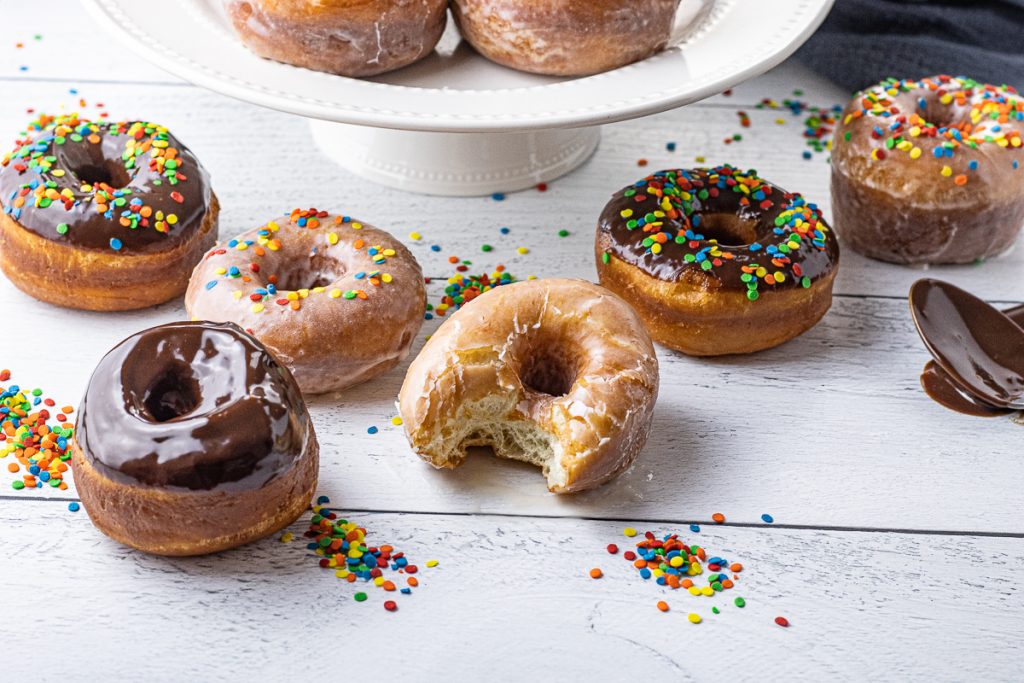 chocolate and glazed donuts, one with a bite out of it and some with colorful sprinkles