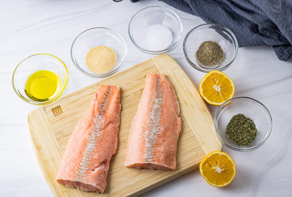 frozen salmon fillets on a wooden cutting board surrounded by small bowls filled with spices