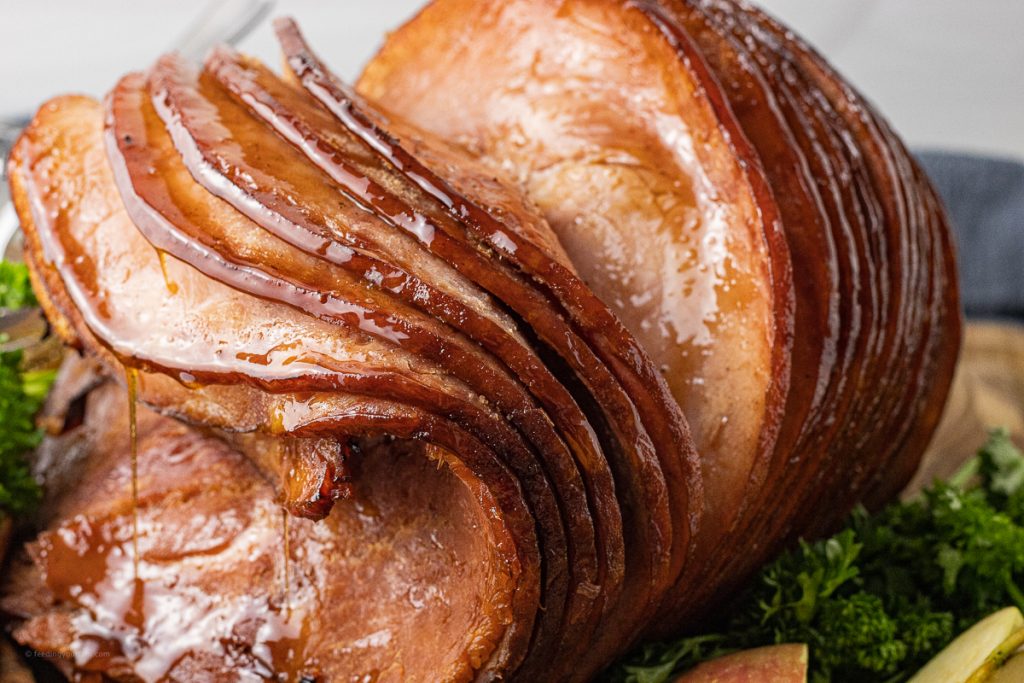sliced ham on a wooden cutting board with dripping glaze coming from the slices