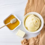 bowl of honey butter with honey and butter cube next to it