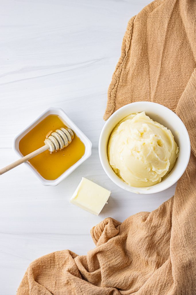 white bowl with honey butter and honey and block of butter next to it