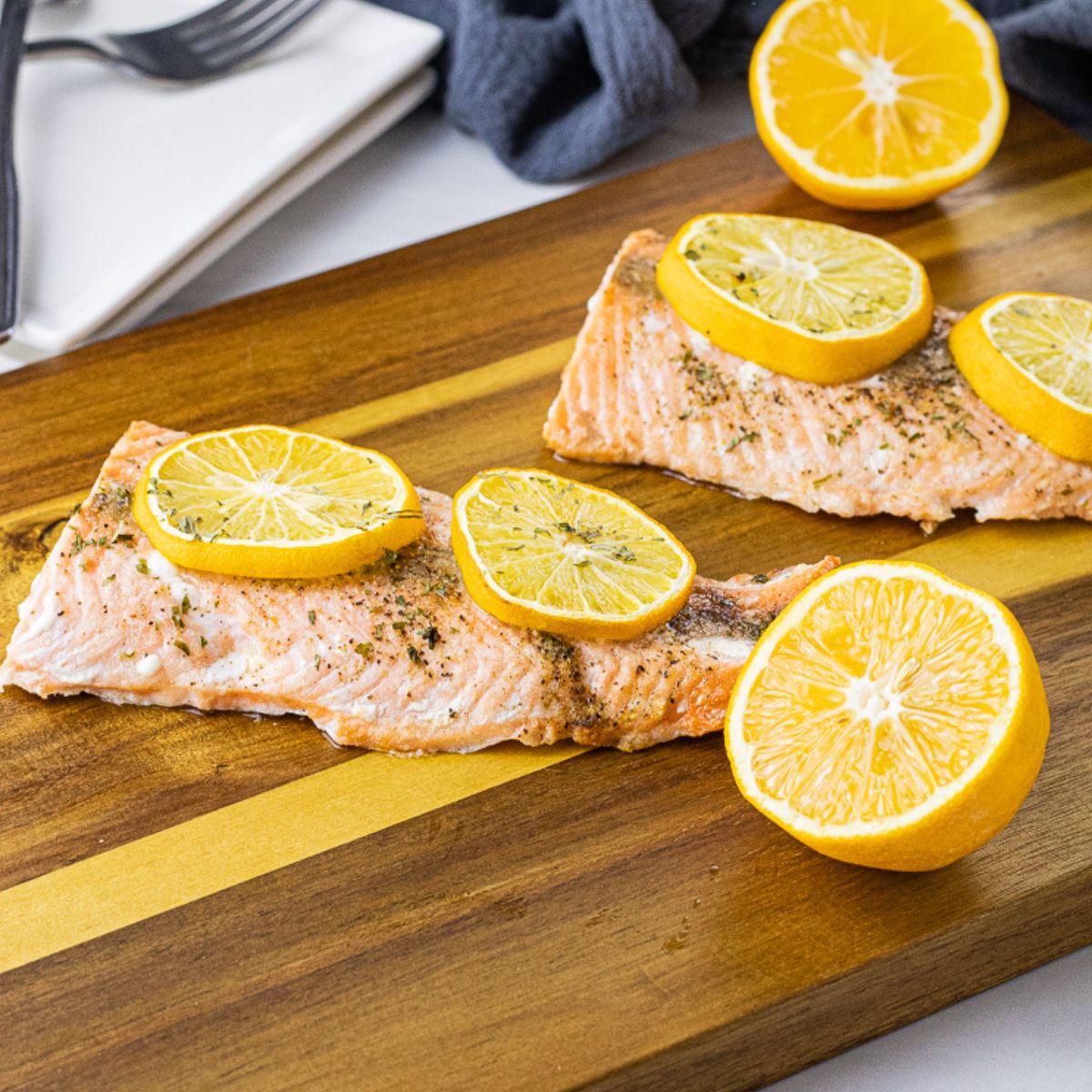 cooked salmon pieces topped with lemon slices on a wooden cutting board