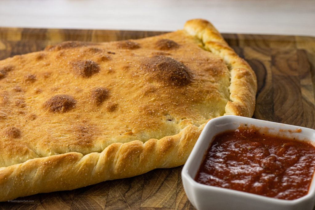 pizza dough and a cooked calzone on a wooden cutting board