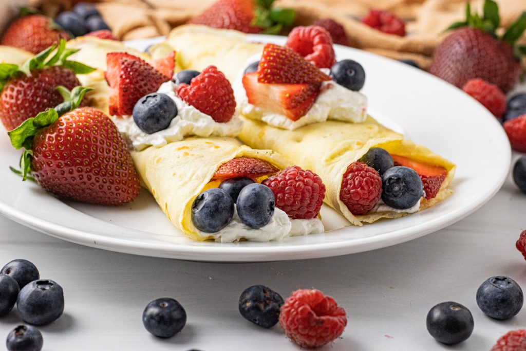 two crepes filled with berries and whipped cream on a white plate
