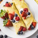 two crepes filled with berries and whipped cream on a white plate
