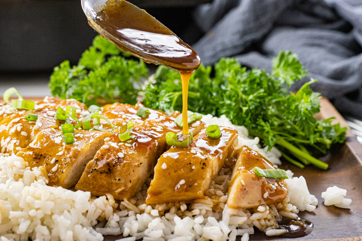 spoon drizzling sauce over sliced chicken that is on rice