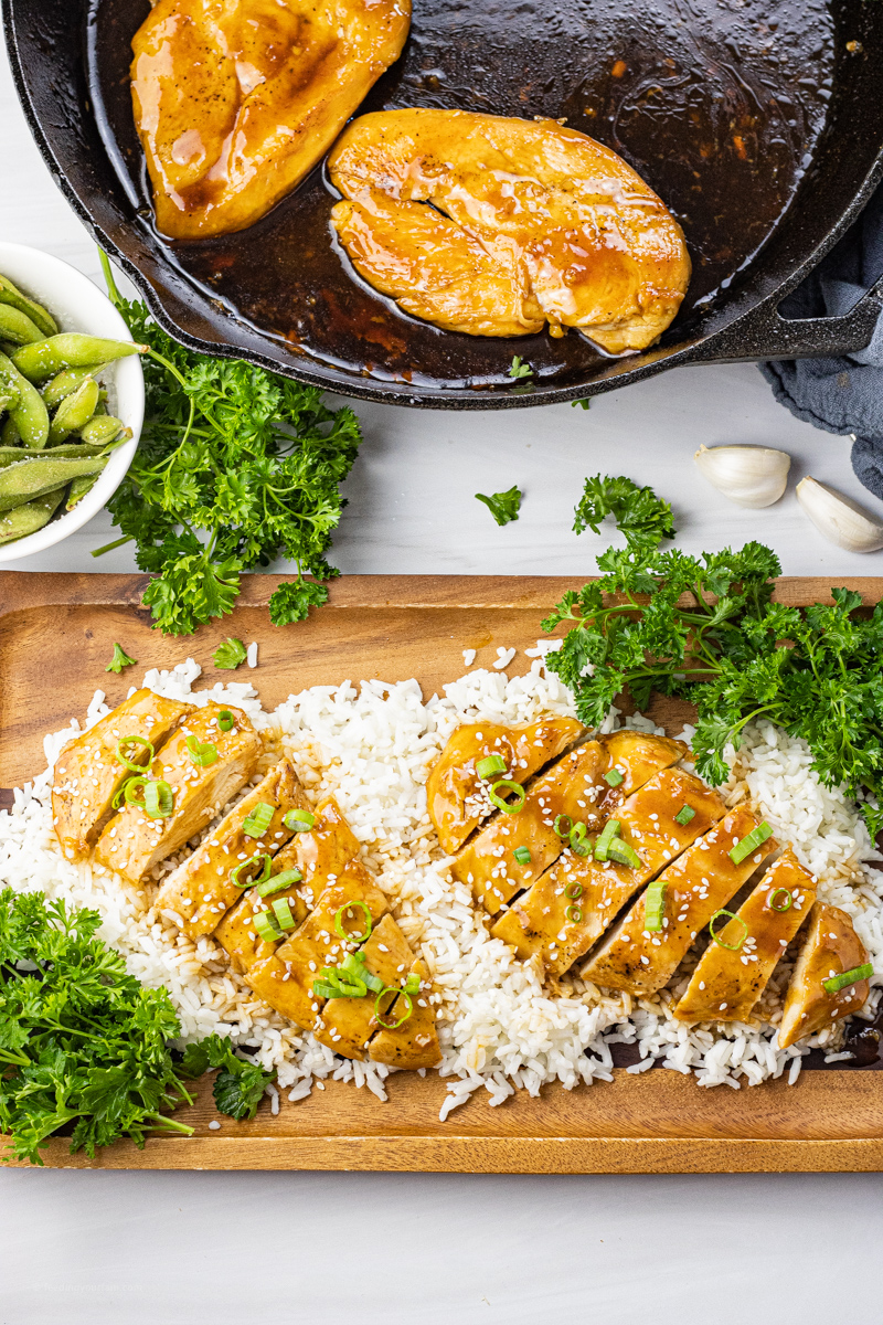 sliced chicken with a sticky honey sauce topped with sliced green onions and sesame seeds over rice