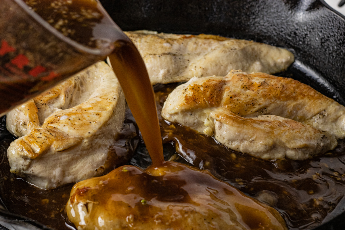 a cup pouring sauce over cooked chicken in a pan