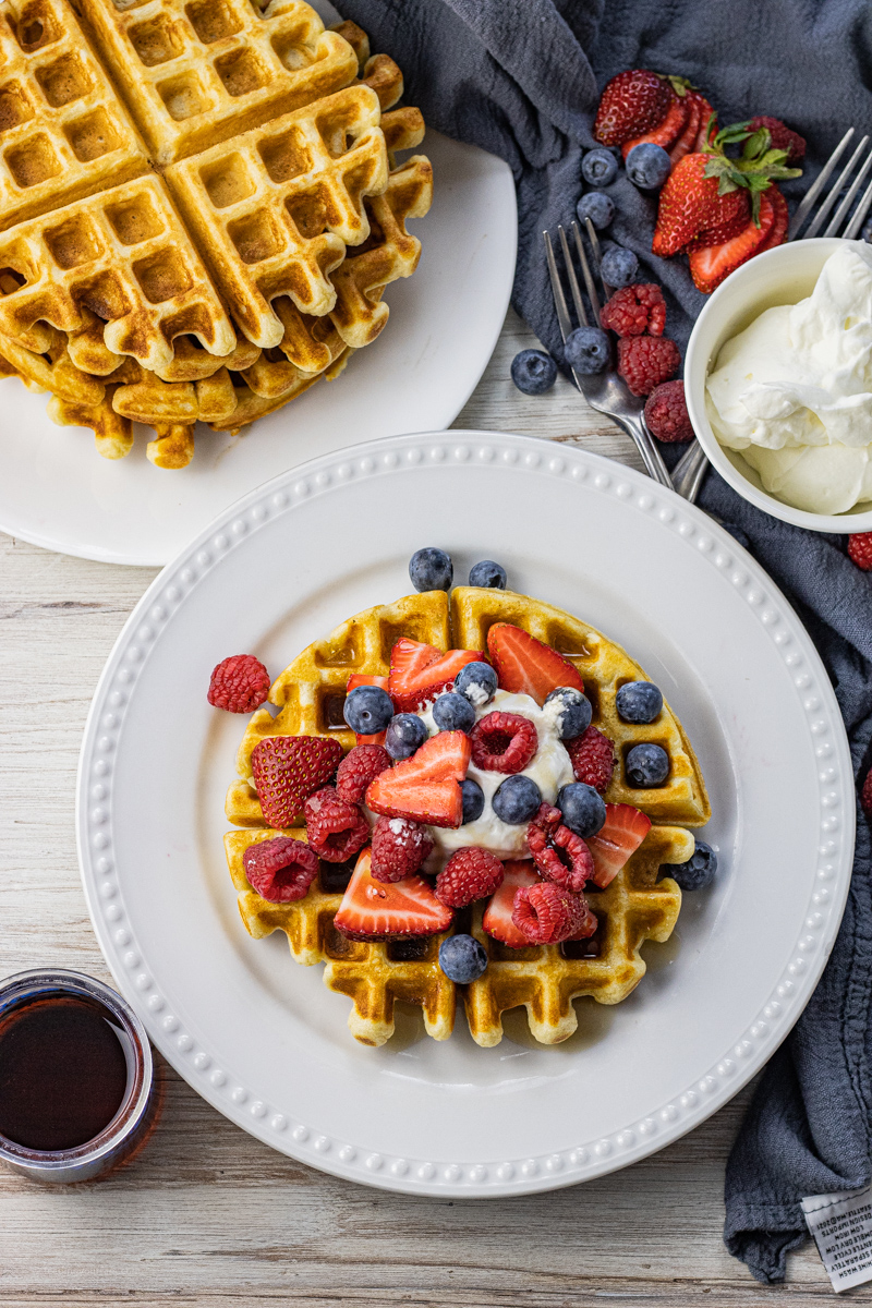 waffle topped with whipped cream, berries and syrup on a white plate