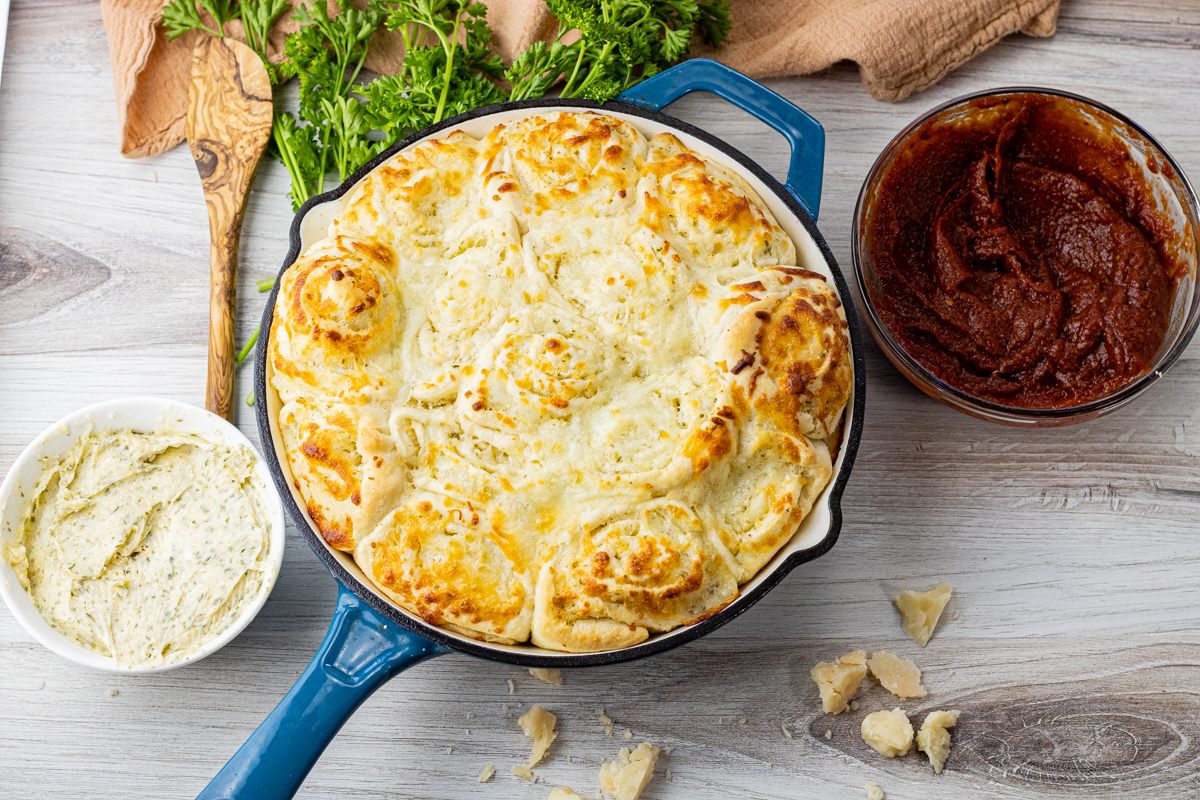 cast iron pan filled with cheesy rolls with garlic butter and pizza sauce next to the pan
