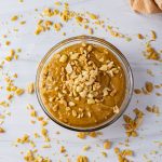 bowl of peanut butter sauce with chopped peanuts on top