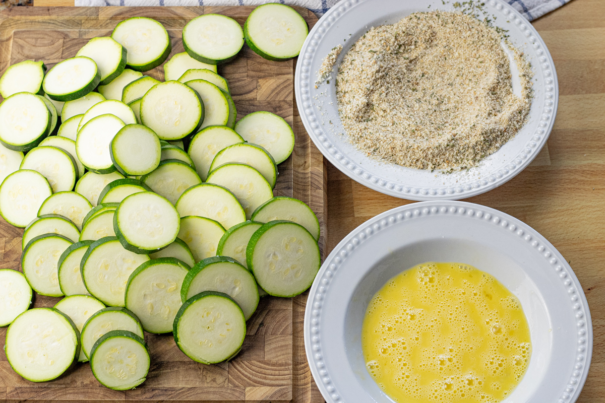round zucchini pieces next to two bowls, one with beaten egg and the other with breadcrumbs
