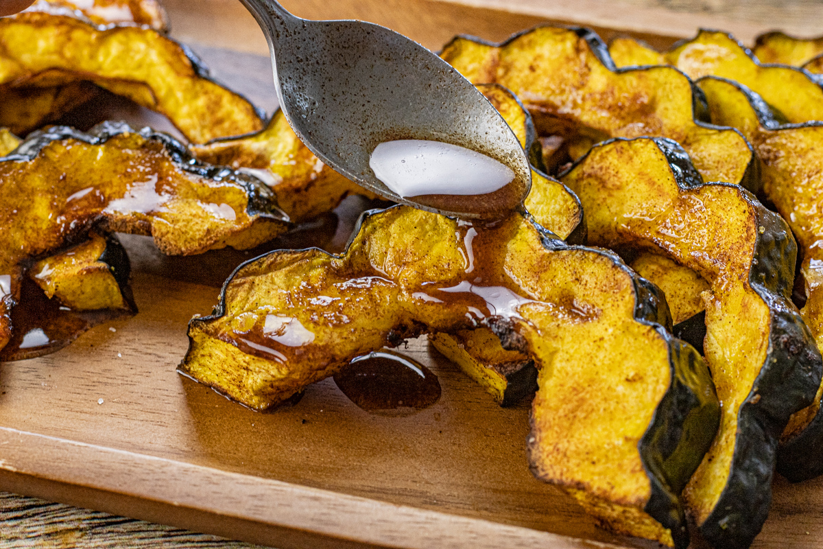 spoon drizzling cinnamon butter over cooked acorn squash slices