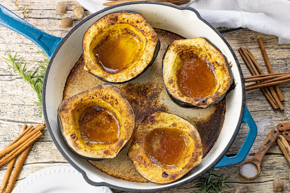 four halves of acorn squash in an enameled cast iron pan filled with melted butter, brown sugar and spices