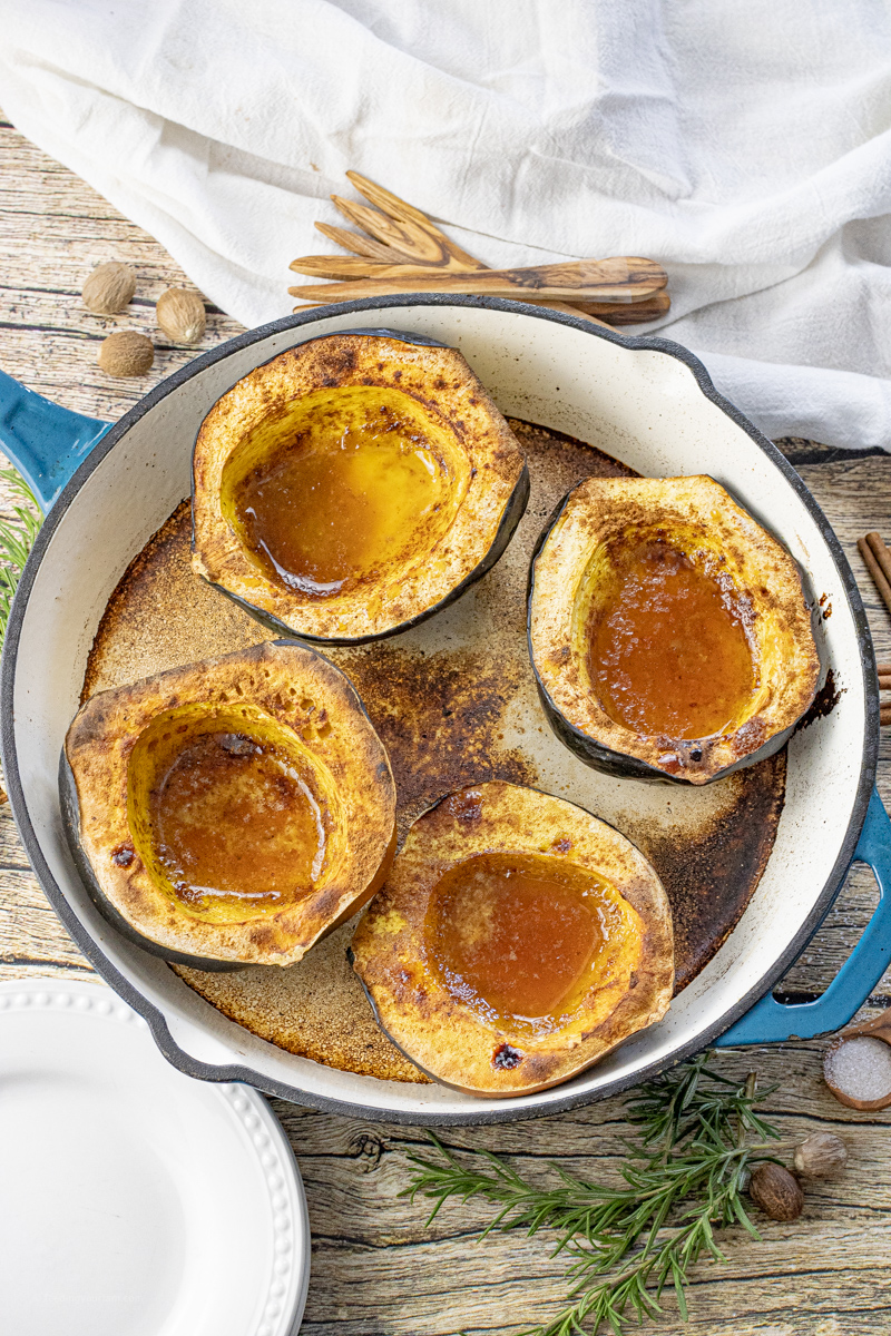 four acorn squash halves in an enameled cast iron pan filled with melted butter and spices