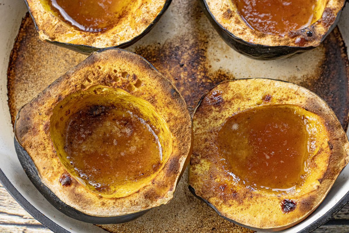 oven baked acorn squash in a skillet filled with melted butter and brown sugar and spices.