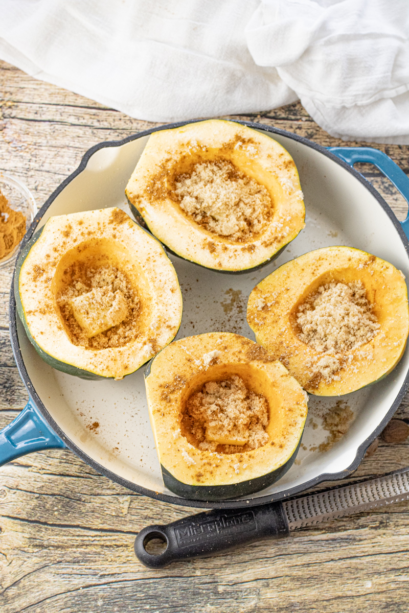 four uncooked halves of acorn squash in an enameled cast iron pan filled with butter, brown sugar and spices.