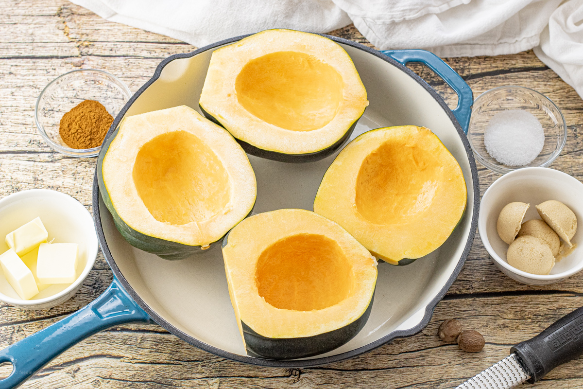 four acorn squash halves uncooked in an enameled cast iron skillet