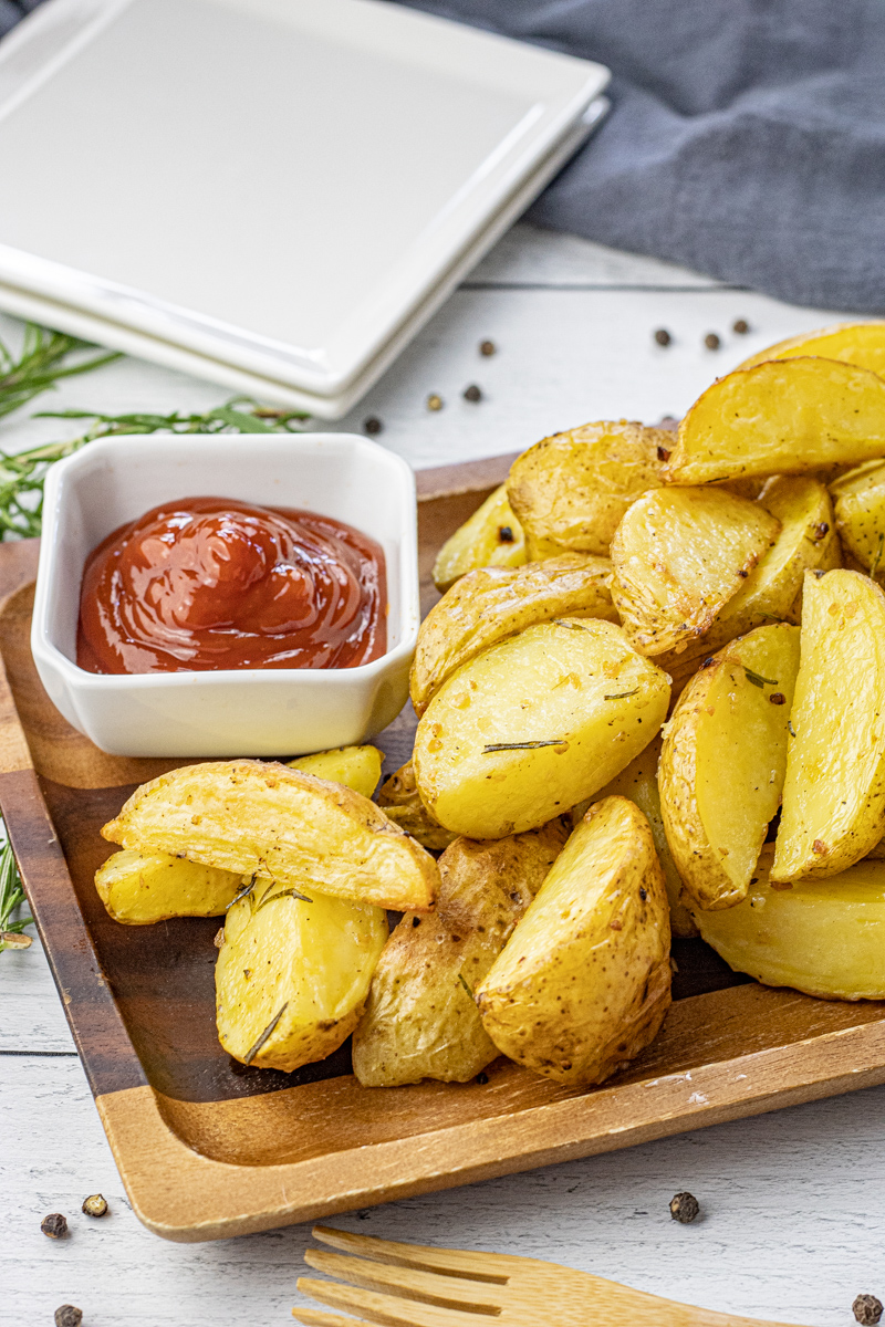 golden potato wedges on a wooden platter with a bowl of ketchup