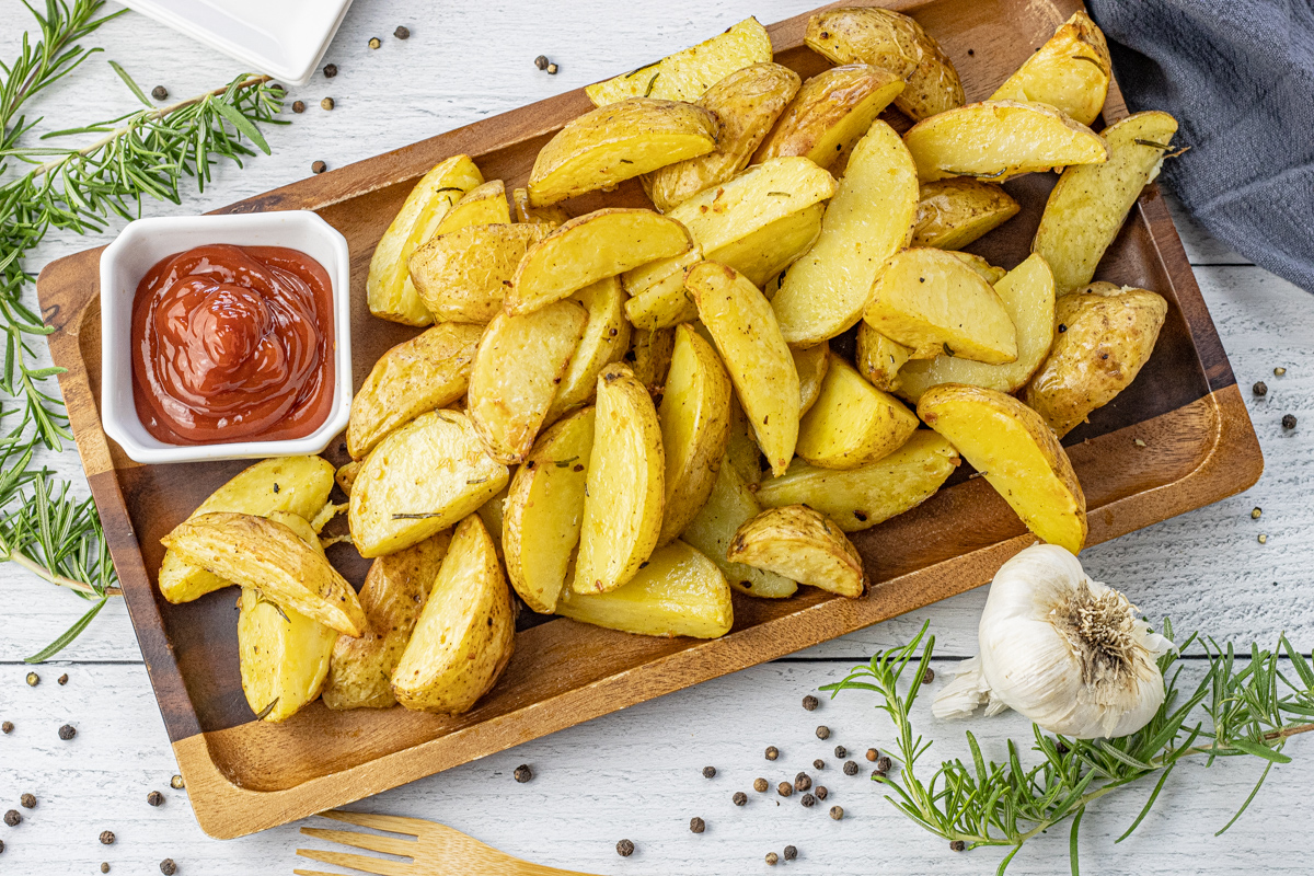 gold potato wedges on a wooden serving platter with a bowl of ketchup