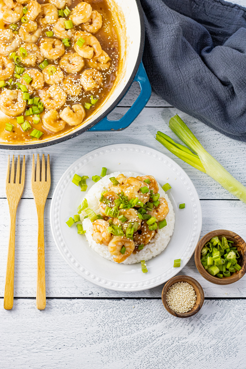 pan filled with shrimp in a teriyaki sauce with a plate on the side that has rice topped with the shrimp