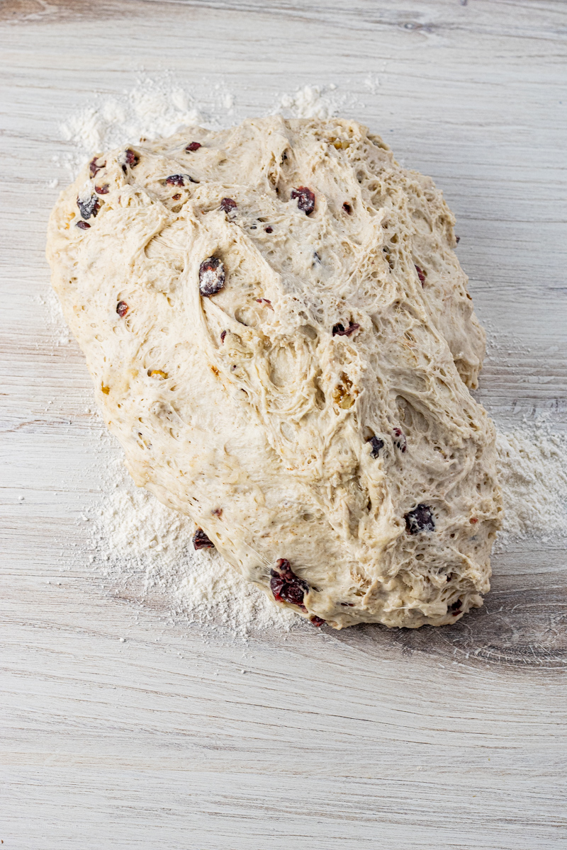 Risen bread dough with cranberries and walnuts on a floured surface, ready to be shaped.
