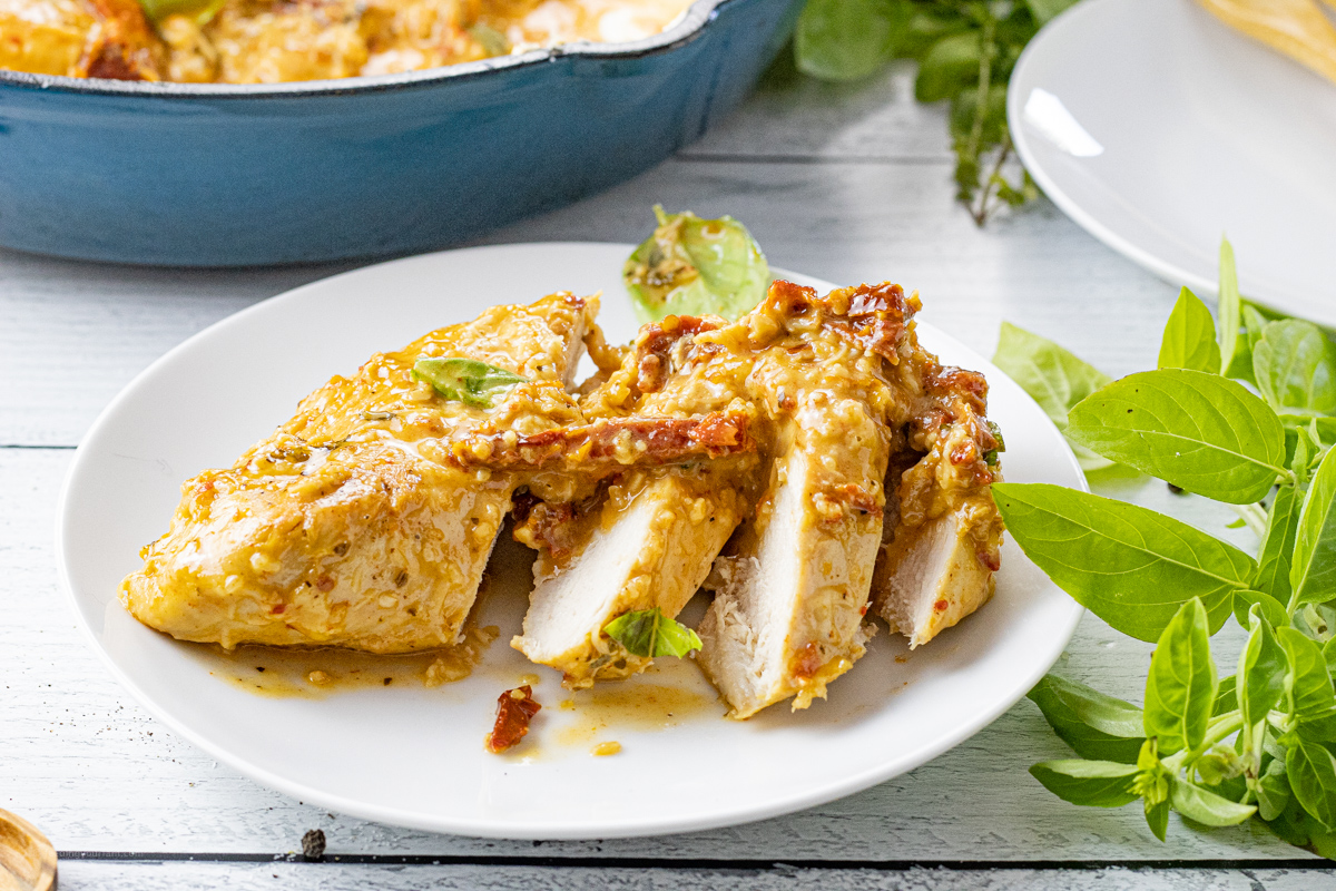 sliced chicken breast on a white plate with creamy tomato sauce over the top