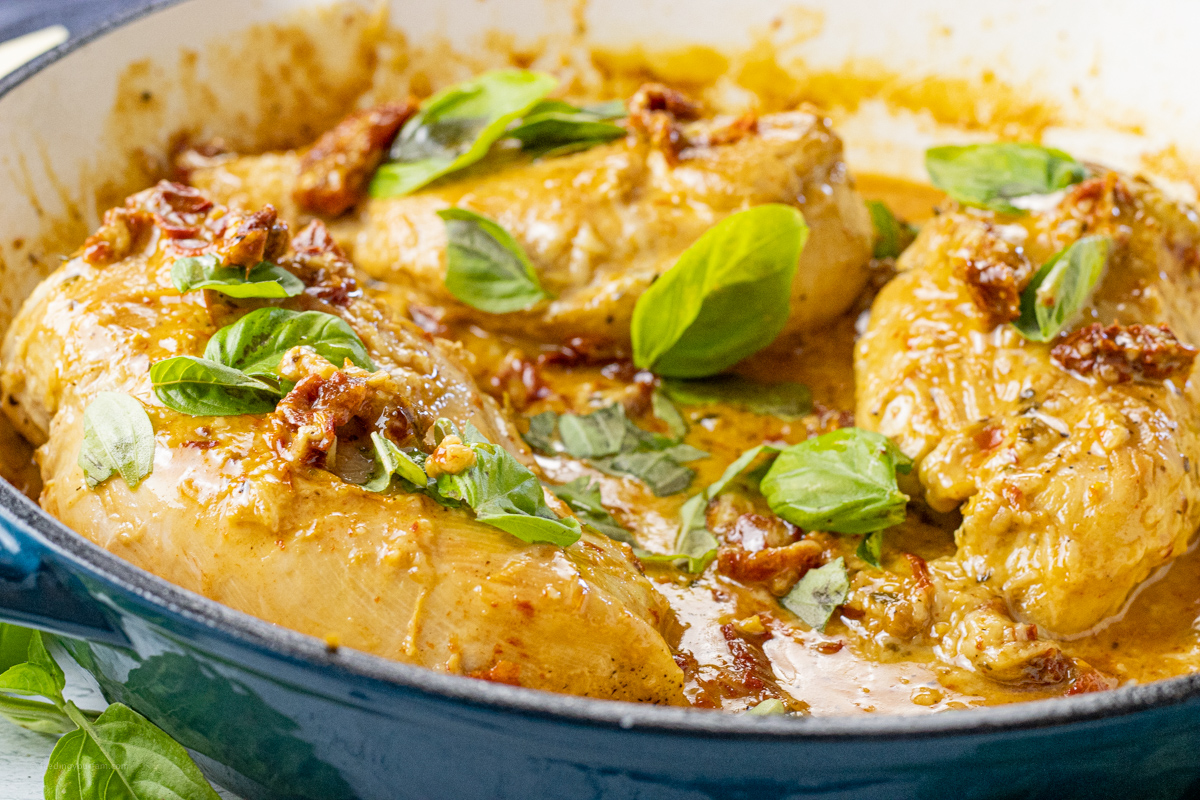 chicken breasts in a pan topped with fresh basil and sun dried tomatoes
