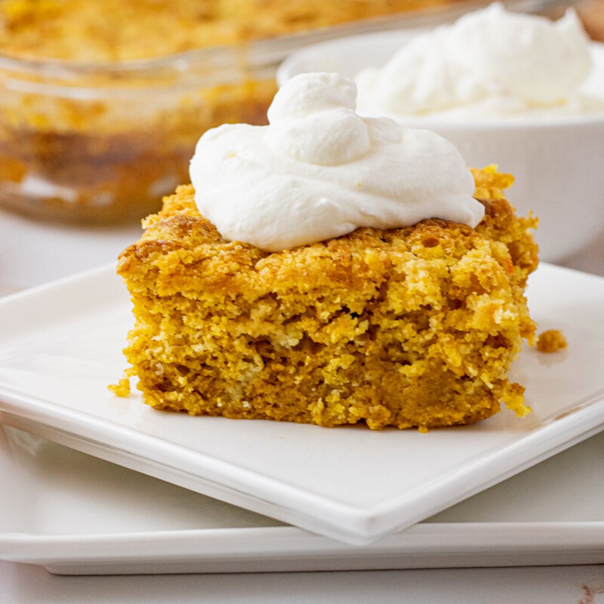 piece of pumpkin cake on a white plate topped with whipped cream