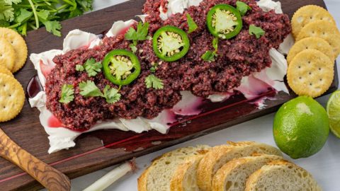 cream cheese topped with salsa made from cranberries on a wooden serving platter