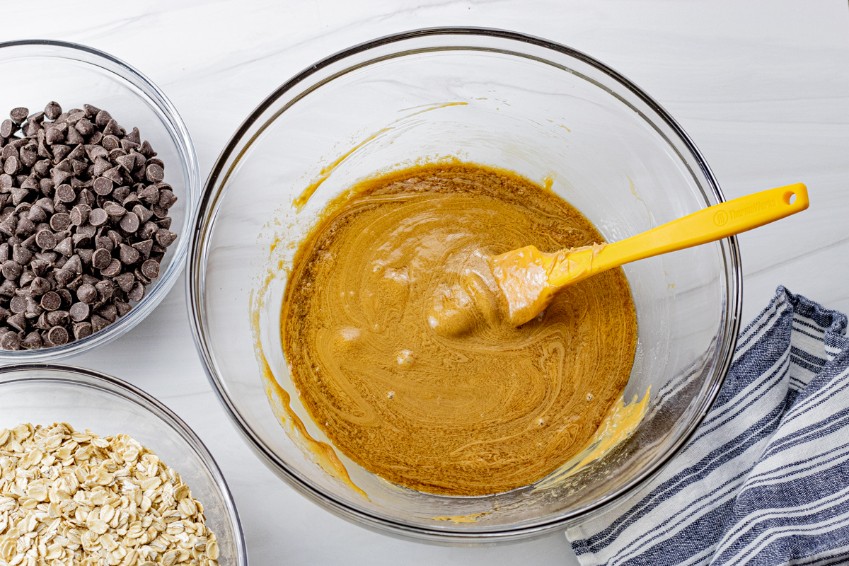 melted peanut butter with vanilla and honey in a large glass mixing bowl with a yellow spatula