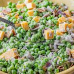 spoon holding up some salad of peas, cheese and bacon