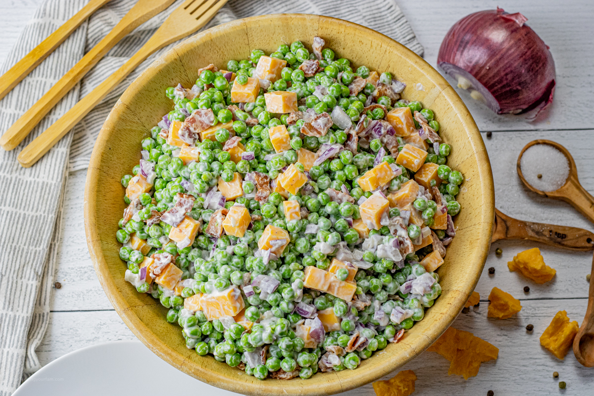 green pea salad with bacon and cheese in a large wooden serving bowl