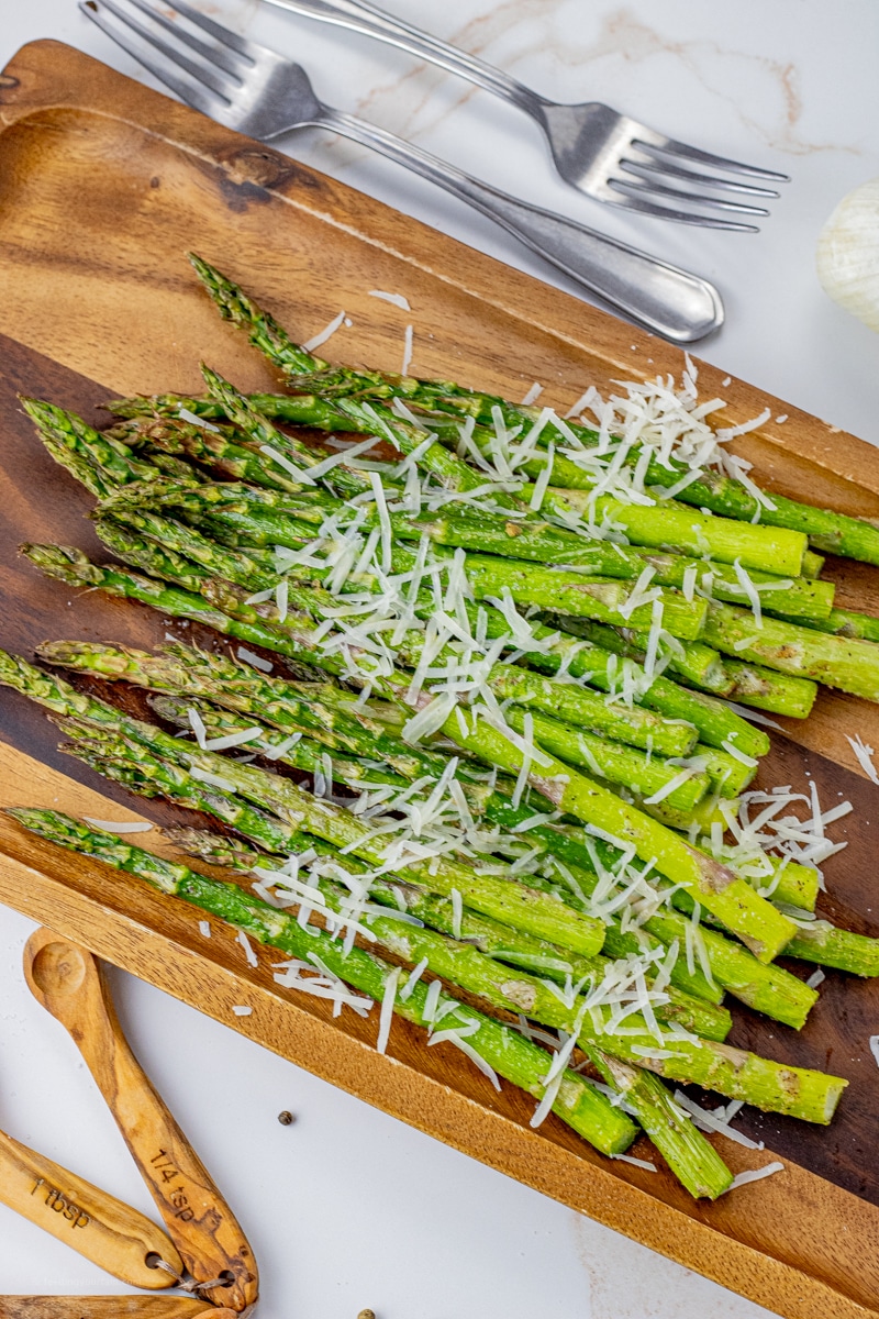 cooked, dark green asparagus on a wooden platter, topped with grated parmesan